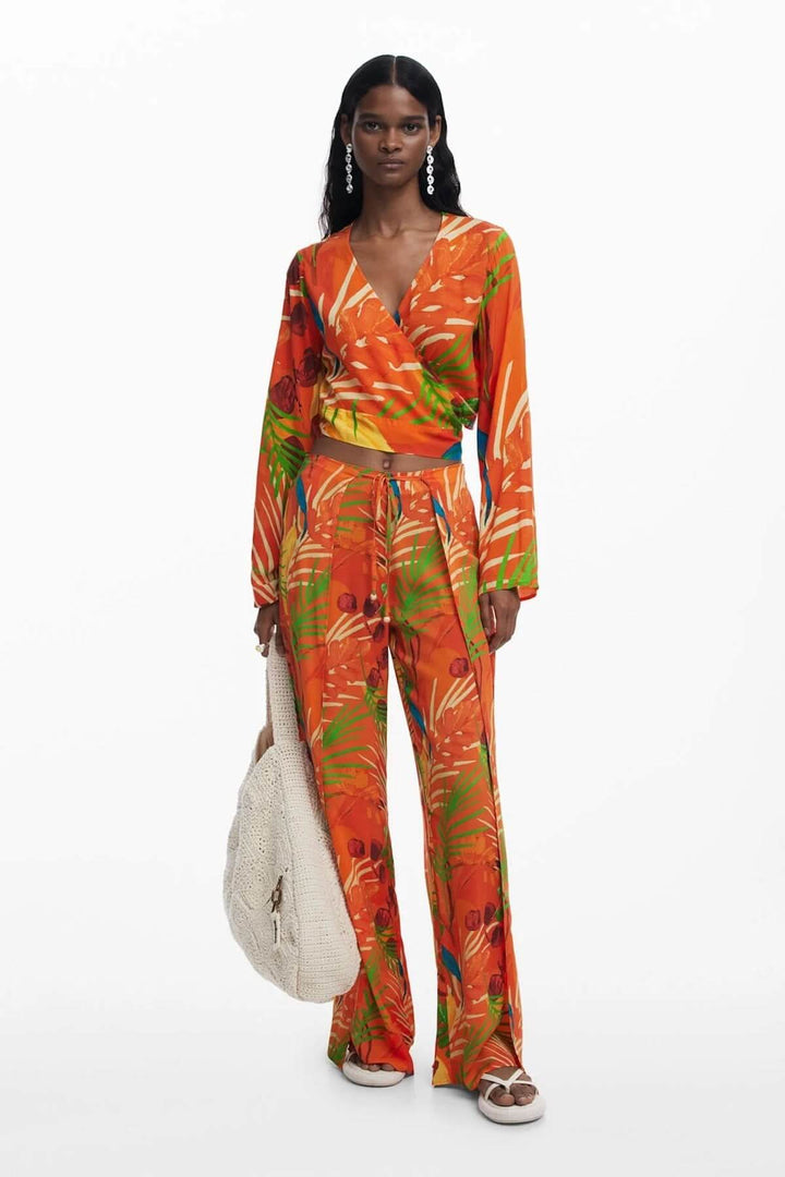 Modèle portant un haut cache-cœur et un pantalon à motifs tropicaux, offrant une allure estivale et élégante.