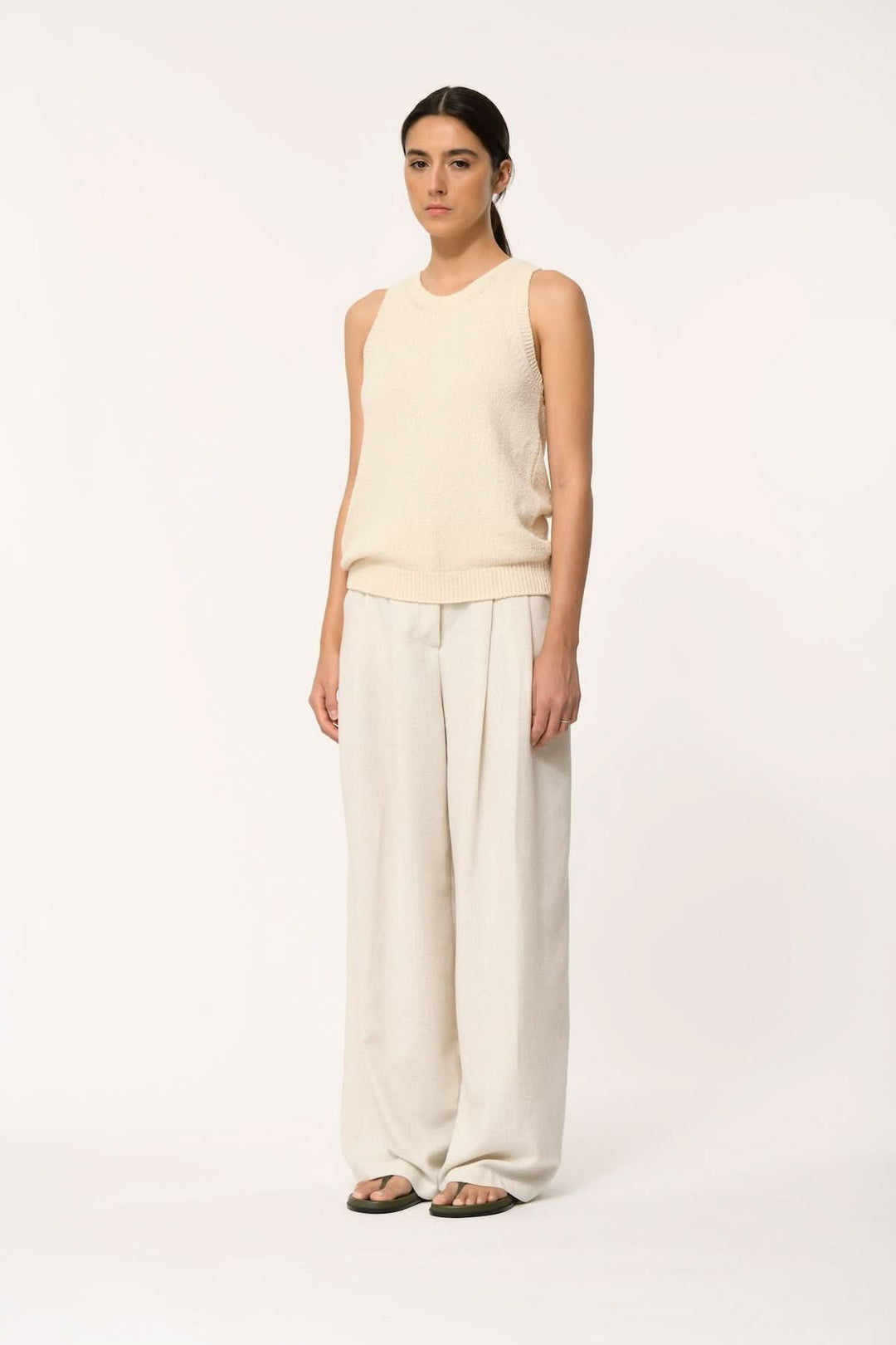 Femme portant le haut sans manches en maille texturée JANICIA, couleur crème, avec un pantalon ample, style minimaliste moderne.