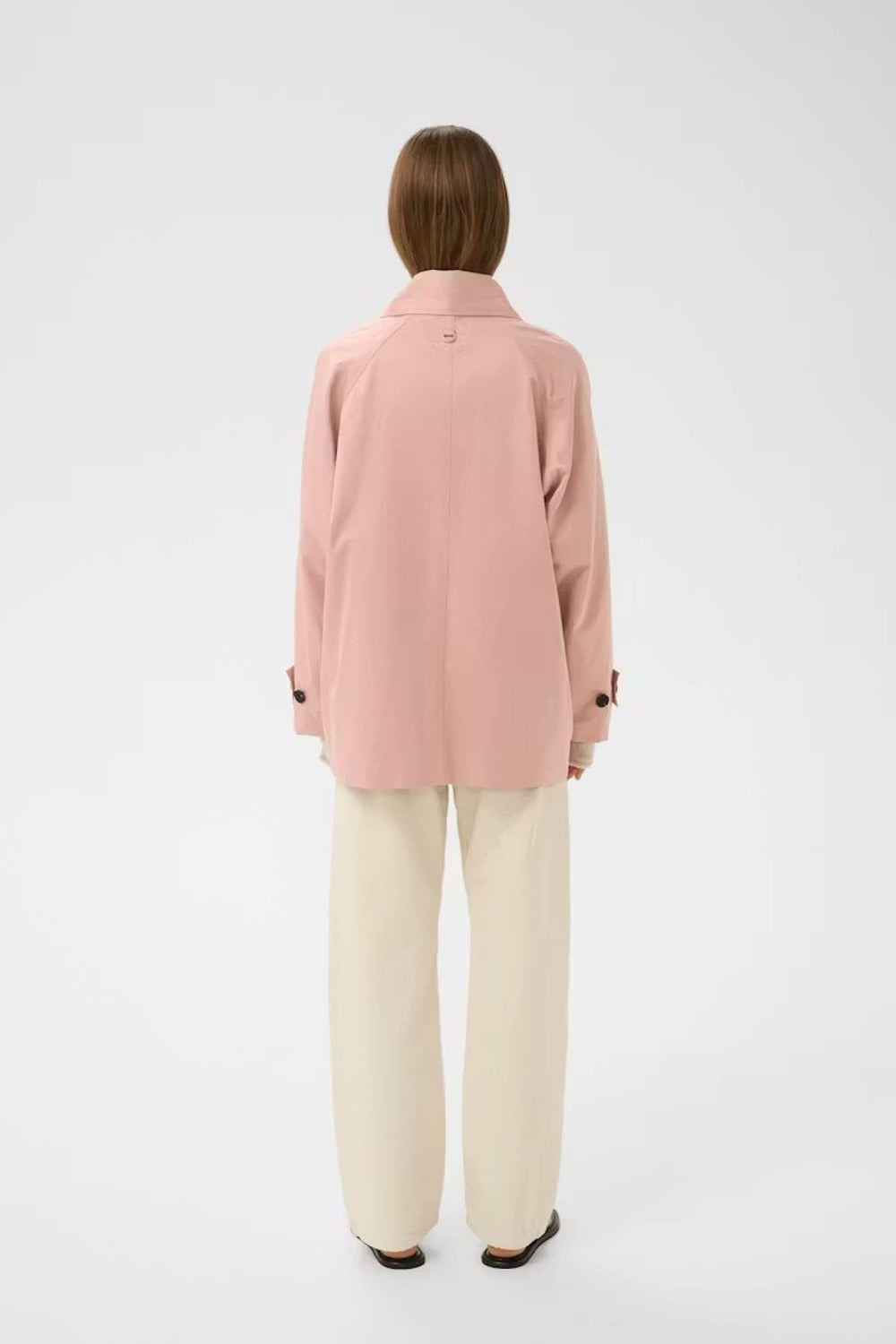 Vue de dos d'une femme portant un imperméable court à col large rose, idéal pour les journées fraîches.