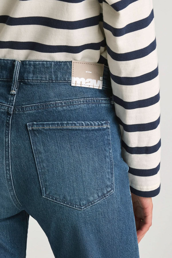 Jean Grace jambe large taille mi-haute en denim bleu avec poche arrière et étiquette de marque, porté par une personne en haut à rayures.