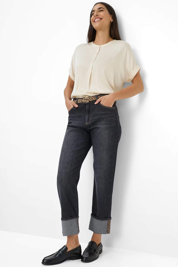 Jean Madison avec revers contrastés, coupe droite, porté avec un haut beige et ceinture imprimée.