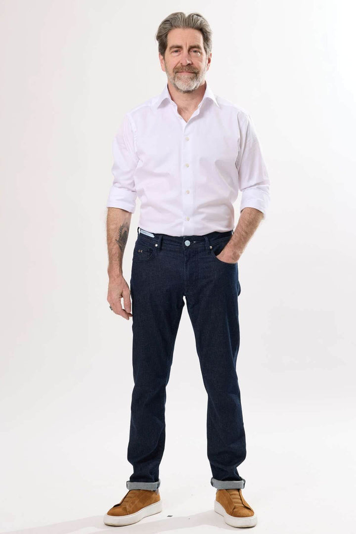 Homme debout en jean coupe droite, chemise blanche, look soigné et décontracté avec des chaussures tendance.