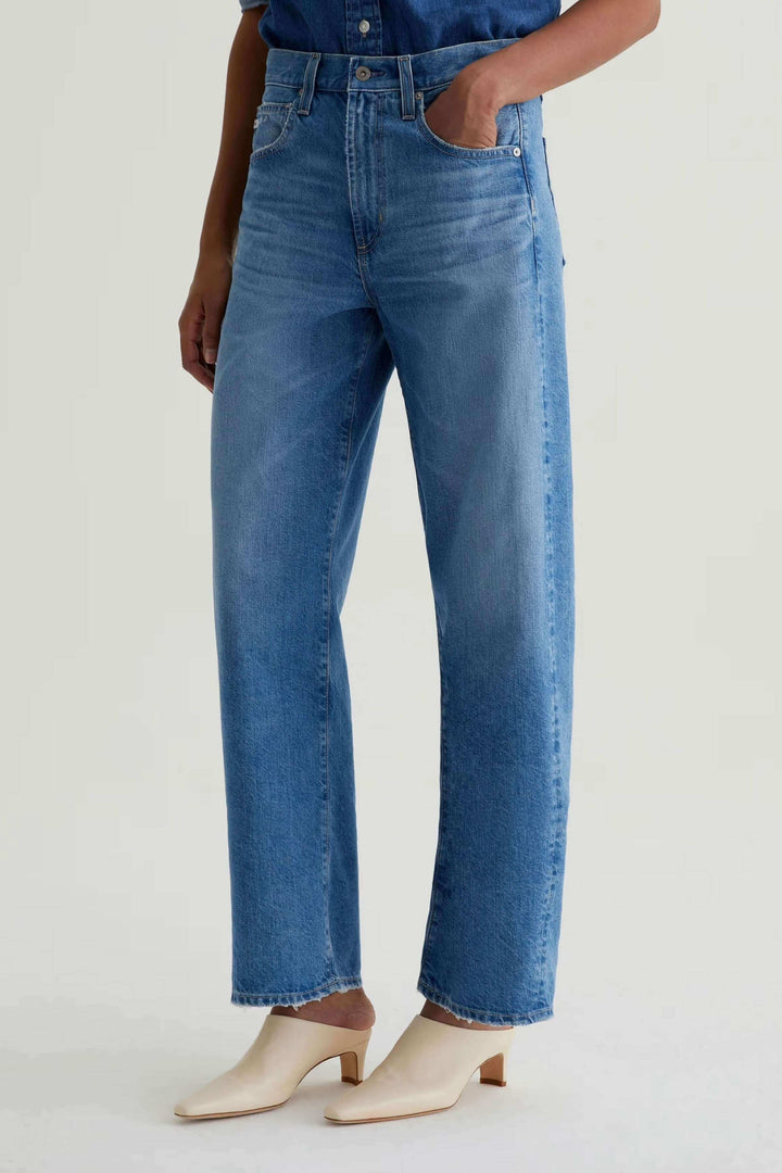 Jean droit à jambe large en coton bleu, taille haute, porté avec des chaussures beige pour un look moderne et décontracté.