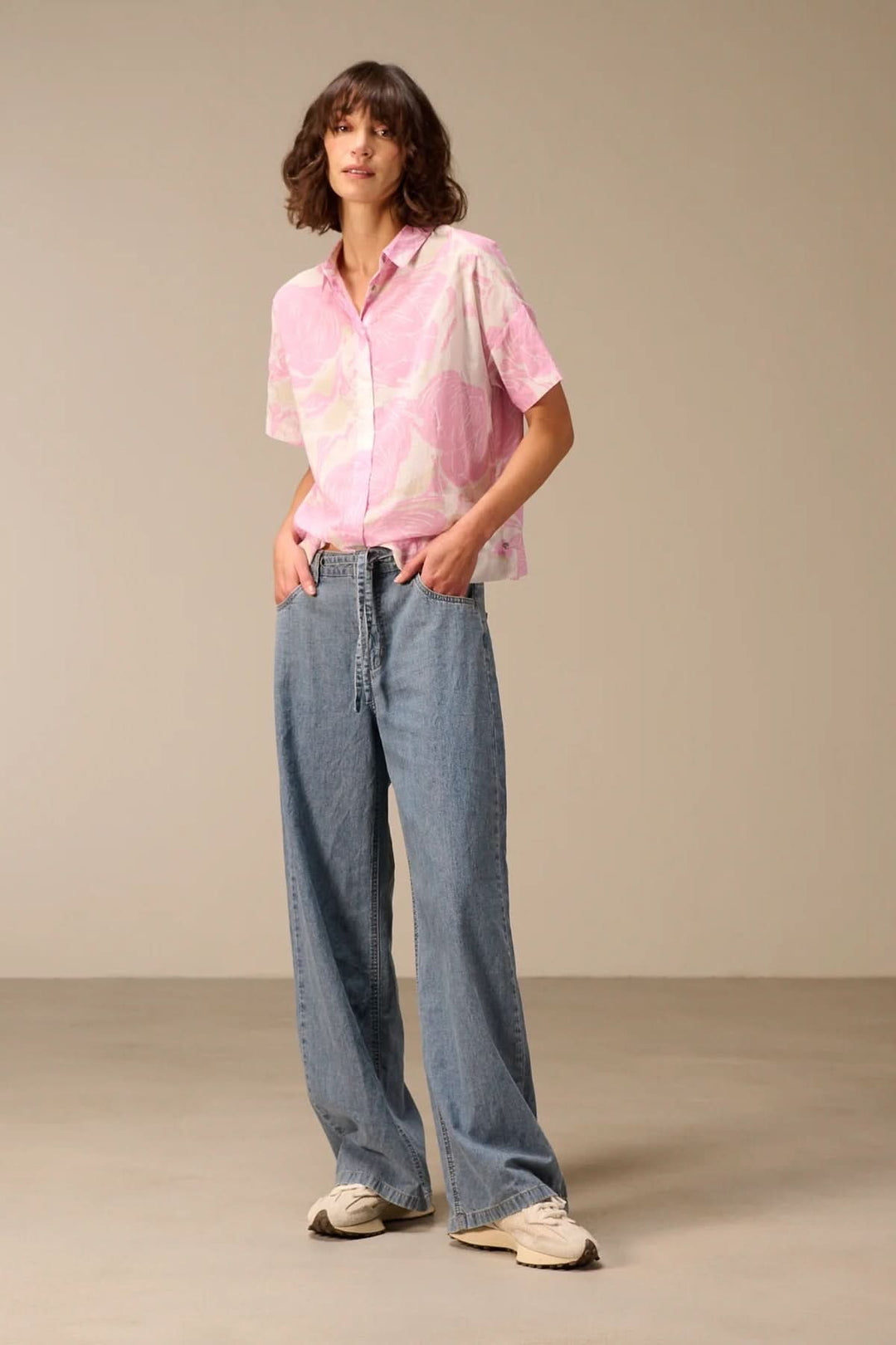 Jean à jambe large avec ceinture à nouer, coupe ample et fluide pour un style moderne et décontracté, porté avec une chemise rose.