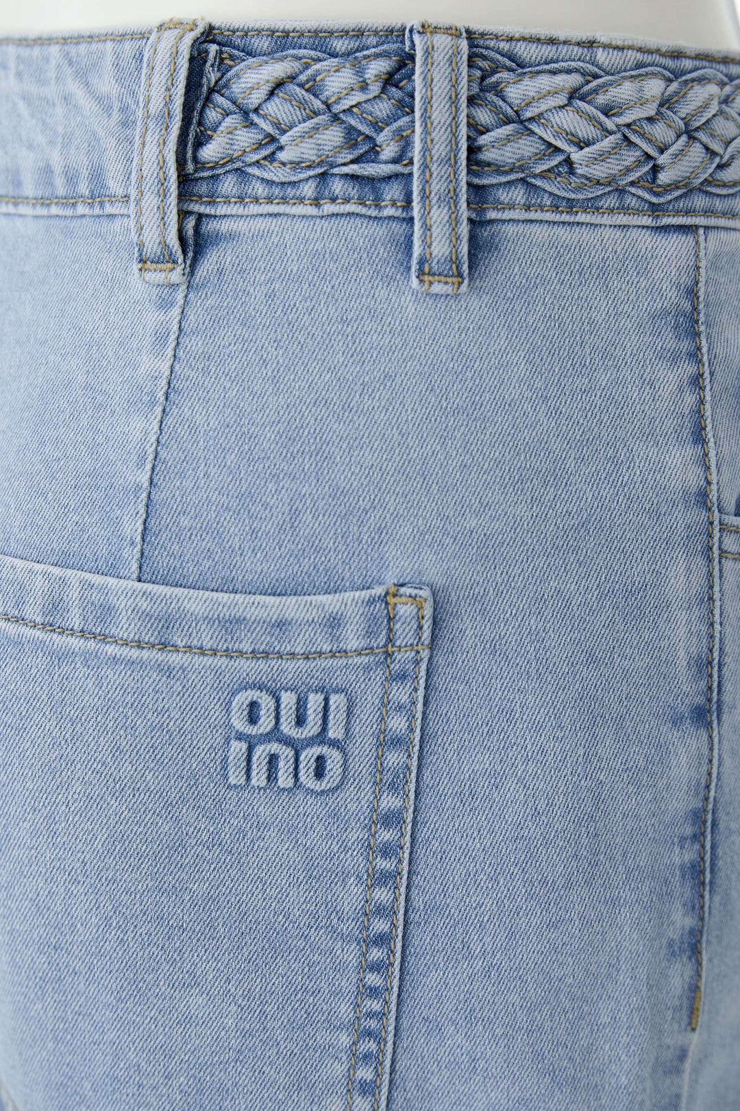 Jean à jambe large avec taille tressée en denim bleu clair, détail de la taille avec tressage élégant.