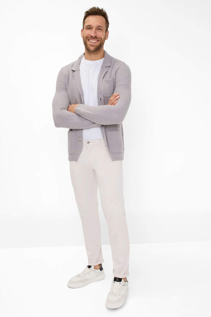 Homme souriant portant un cardigan gris, un t-shirt blanc, et un pantalon clair, parfait pour un look décontracté.