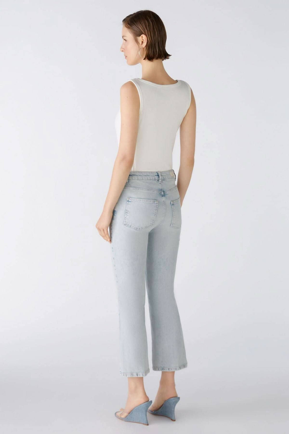 Femme portant un jean évasé en denim clair avec un débardeur blanc, vue de dos.