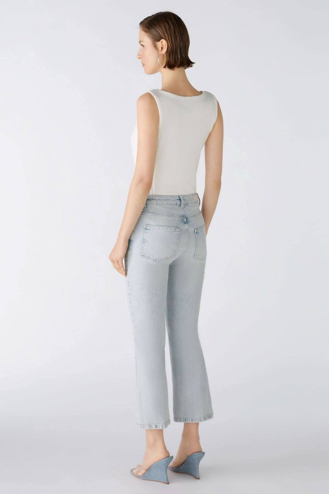 Femme portant un jean évasé en denim clair avec un débardeur blanc, vue de dos.