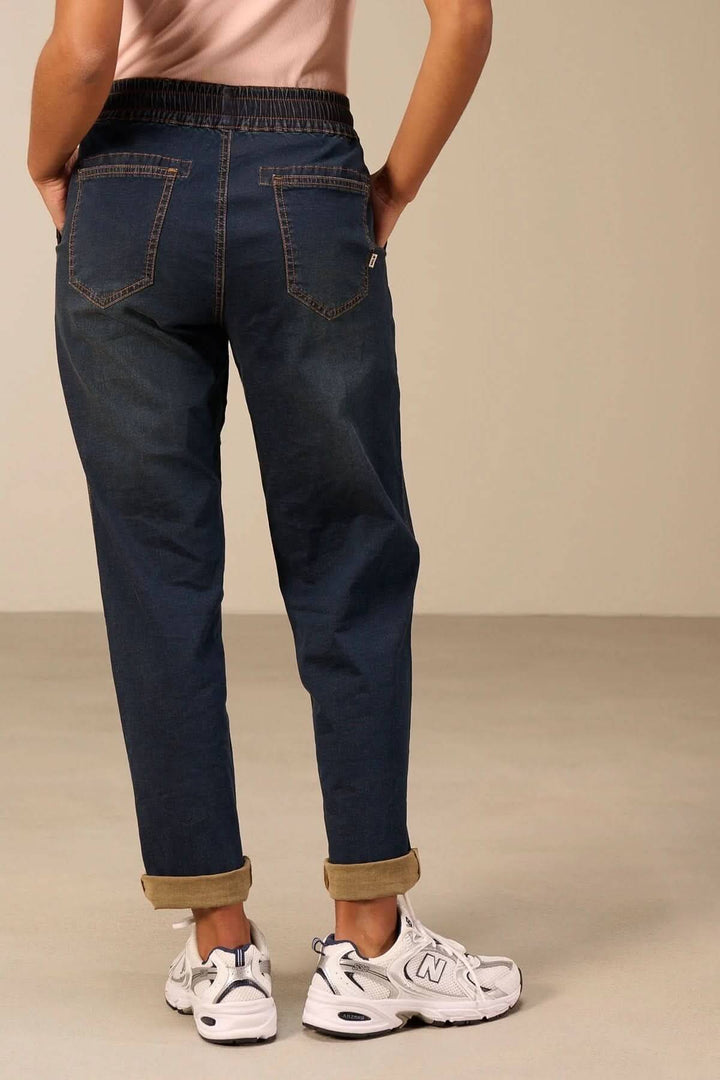 Vue arrière du Jeanjogging à taille élastique, coupe fuselée, poches arrière et bande élastique, porté par une personne avec baskets blanches.