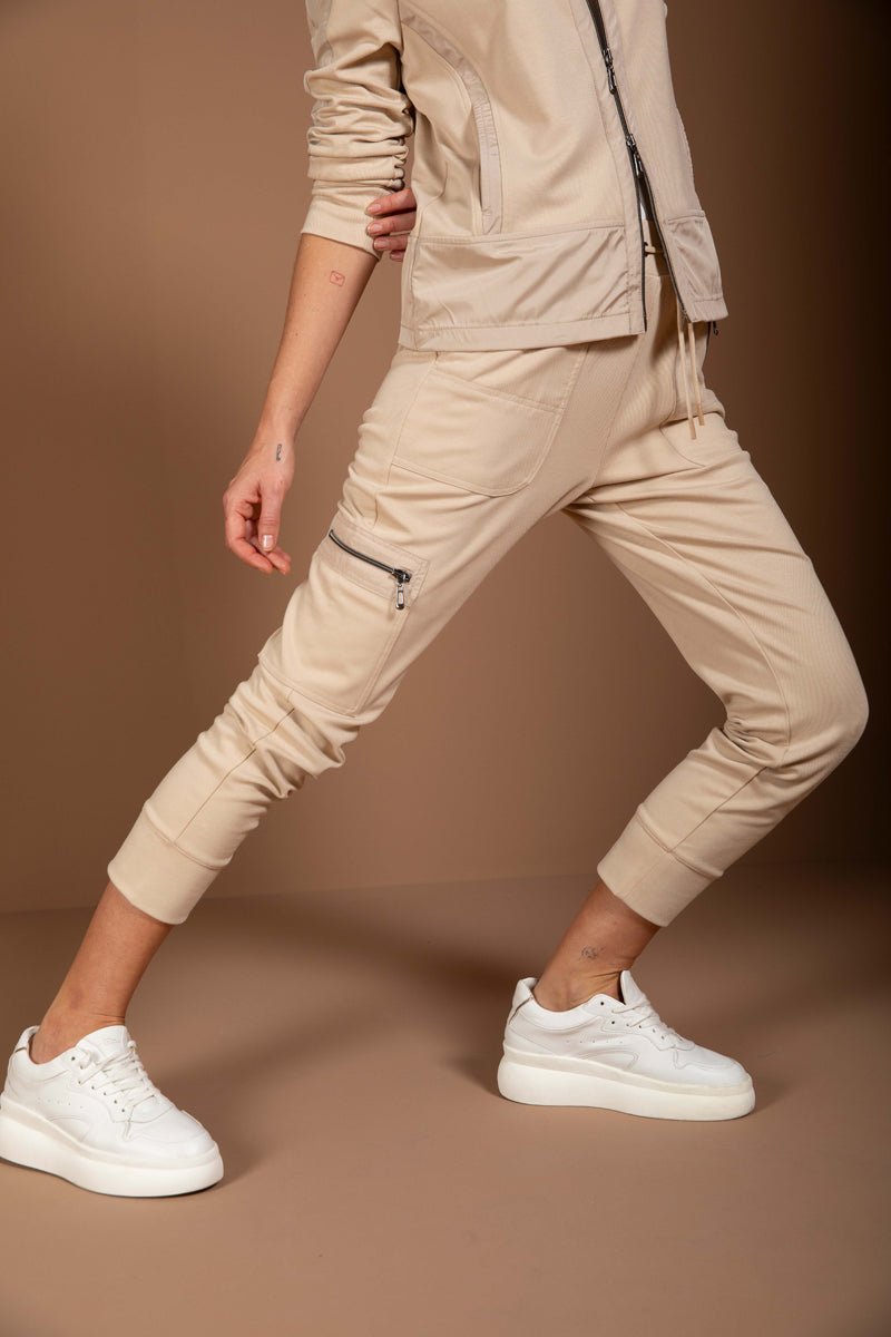 Jogging ajusté beige avec poches zippées et coupe moderne, porté avec des baskets blanches en toile de fond neutre.