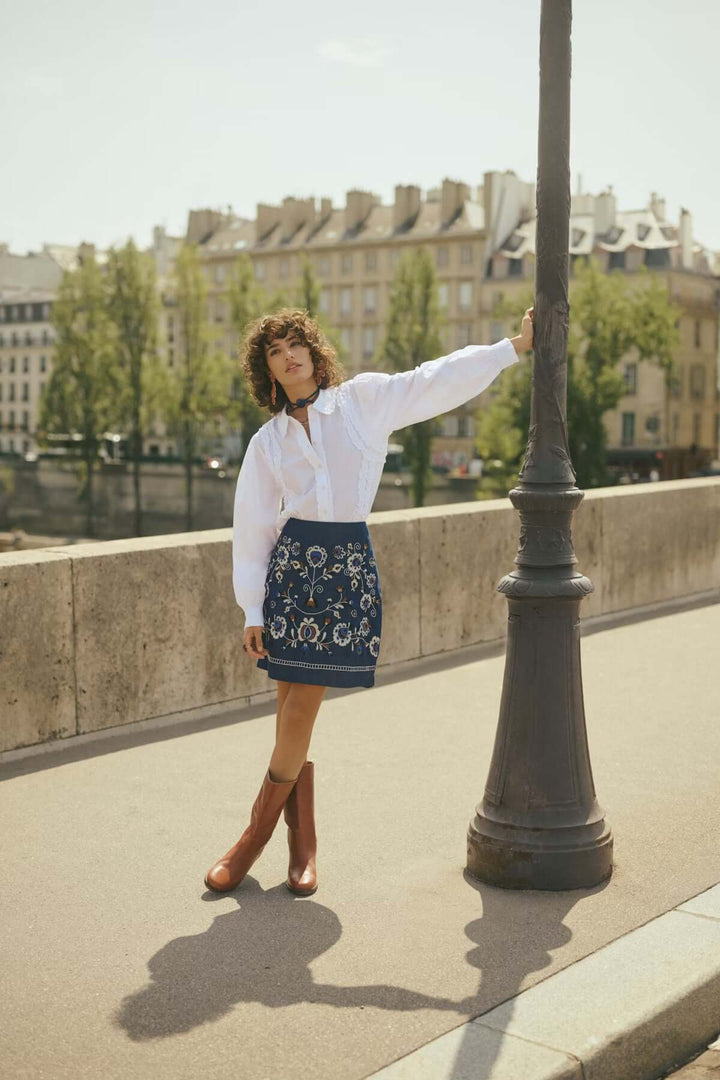 Femme portant une Jupe Gro en denim avec des broderies florales raffinées sur un pont, style bohème chic.