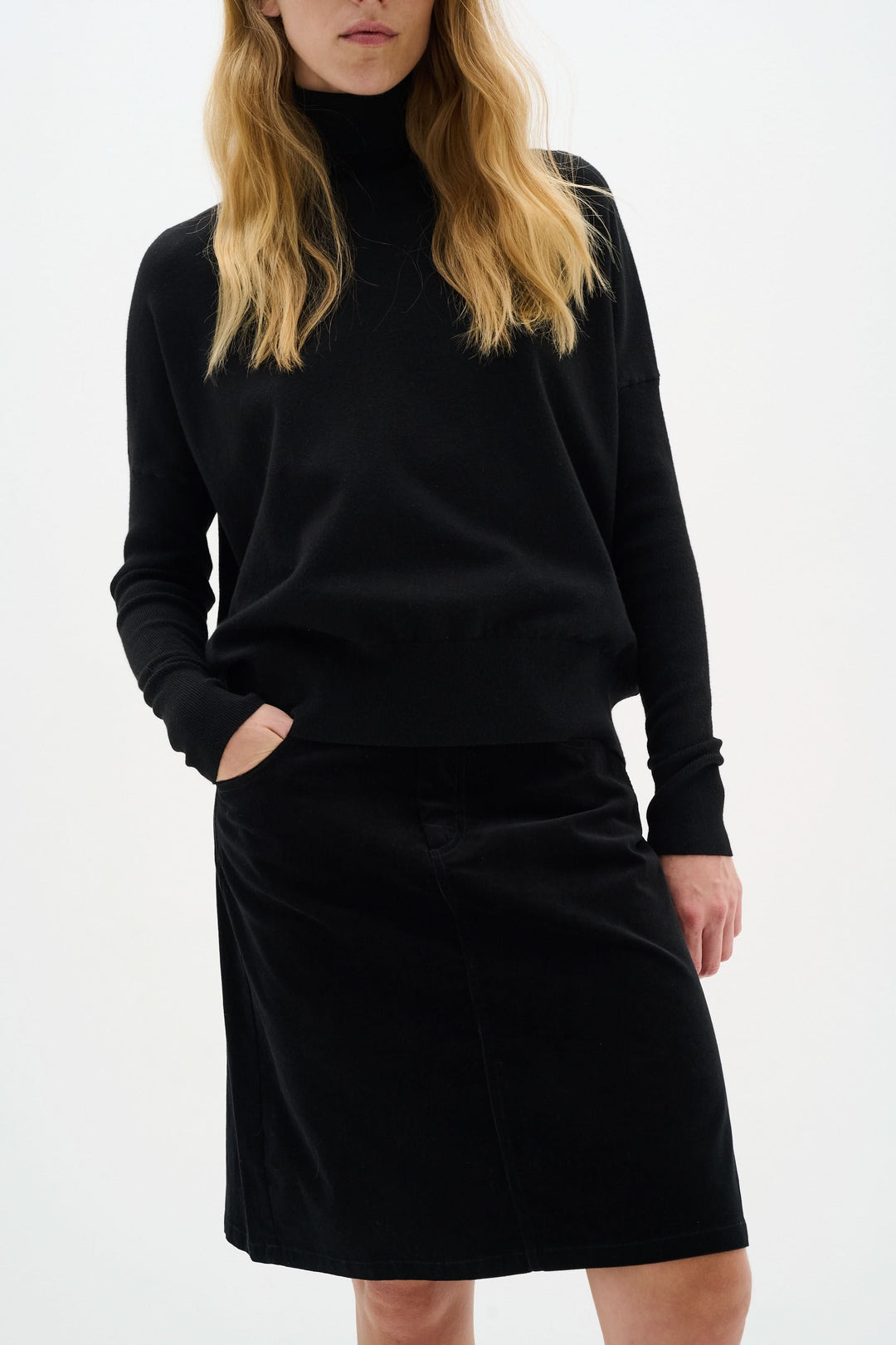 Femme portant une jupe en velours noir avec un haut noir, style moderne et élégant.