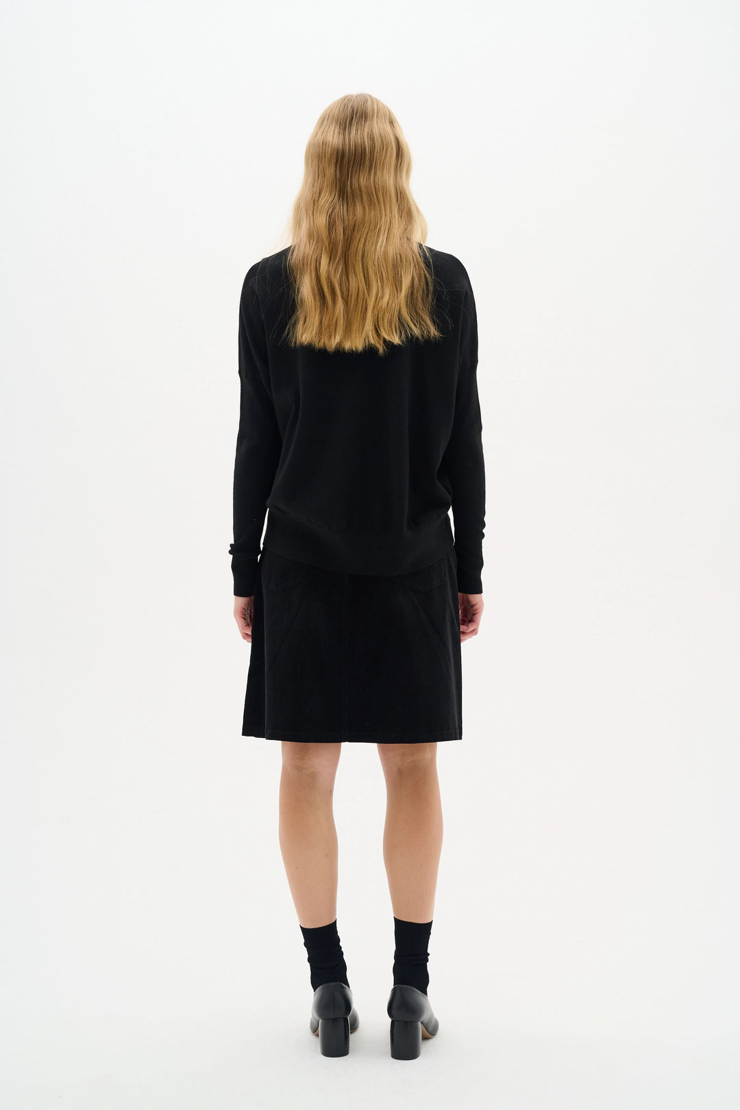 Femme vue de dos portant une jupe en velours noir avec un haut noir, pour un look moderne et élégant.