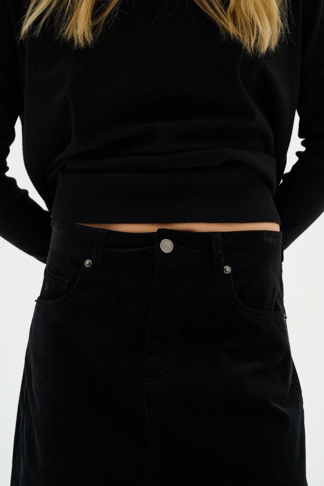 Jupe Rylie en velours noir avec poches et coupe slim, associée à un haut noir. Élégance moderne et ajustée.