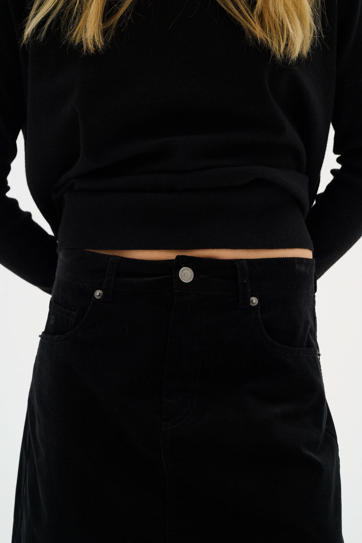 Jupe Rylie en velours noir avec poches et coupe slim, associée à un haut noir. Élégance moderne et ajustée.