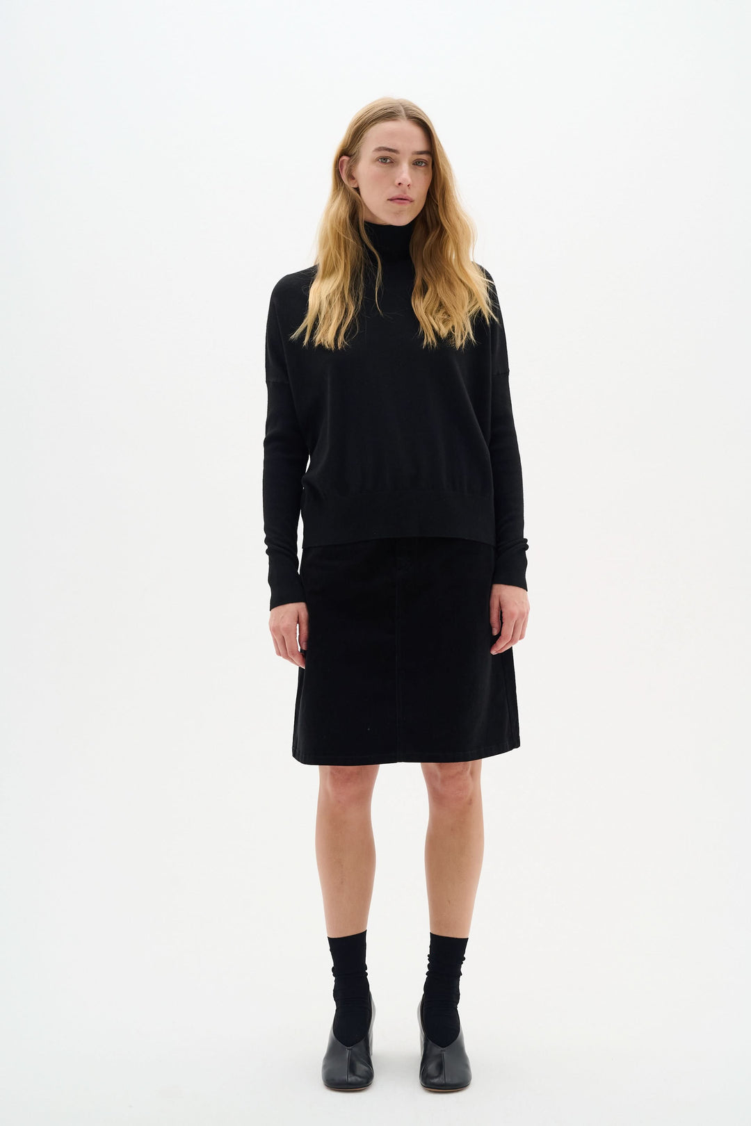 Femme portant une jupe en velours noir, haut noir, avec bottines, style élégant et moderne.