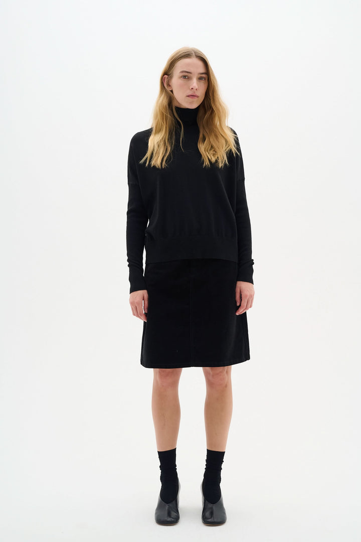 Femme portant une jupe en velours noir, haut noir, avec bottines, style élégant et moderne.