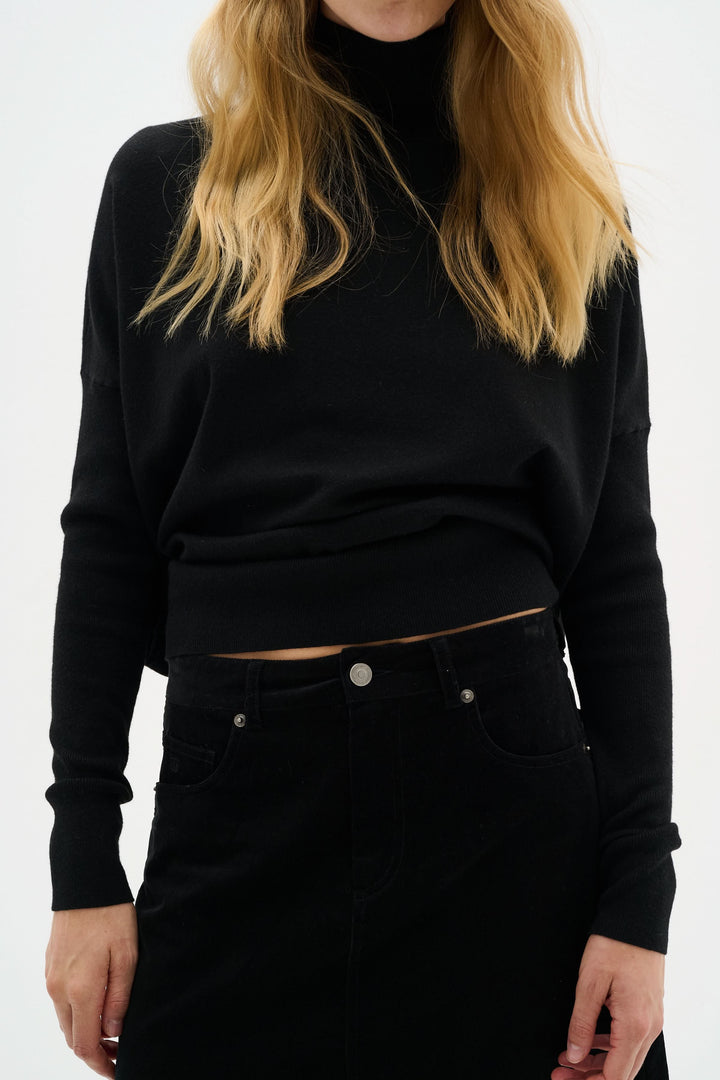 Femme en pull noir col montant et jupe noire, tenue chic et moderne pour les soirées.