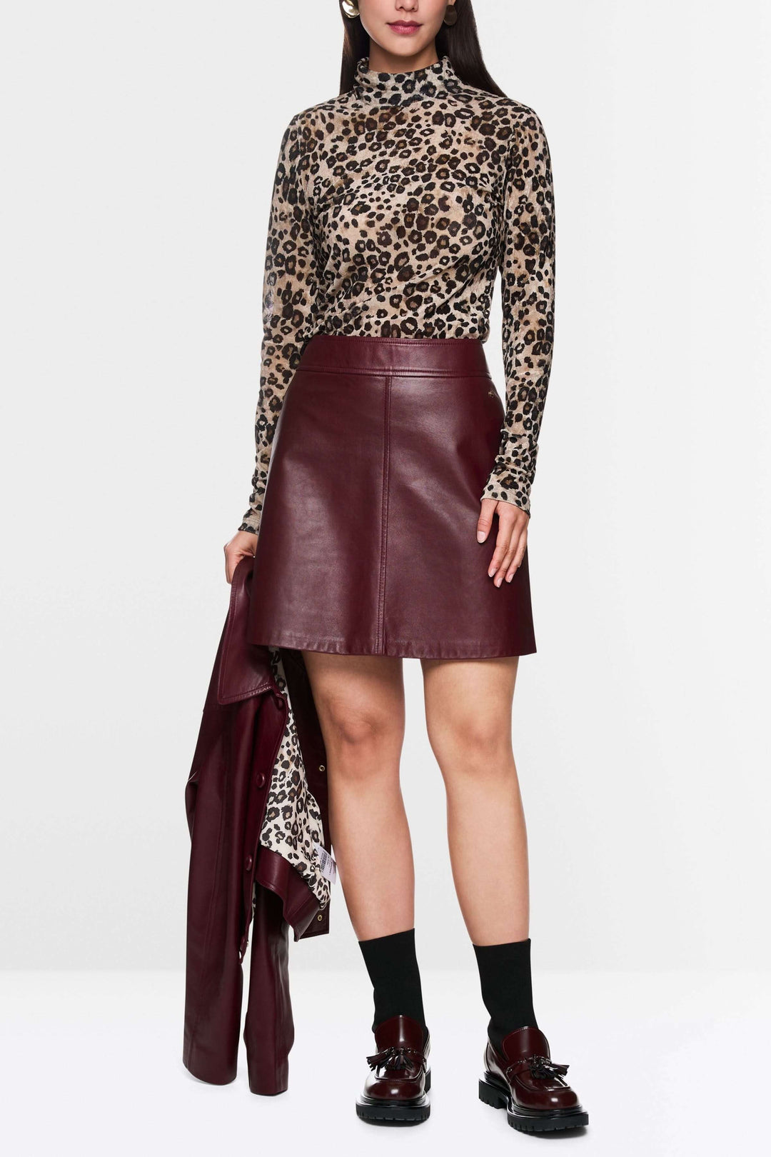 Femme portant une jupe en cuir bordeaux avec un haut à motifs léopard, combinée avec des chaussures noires.