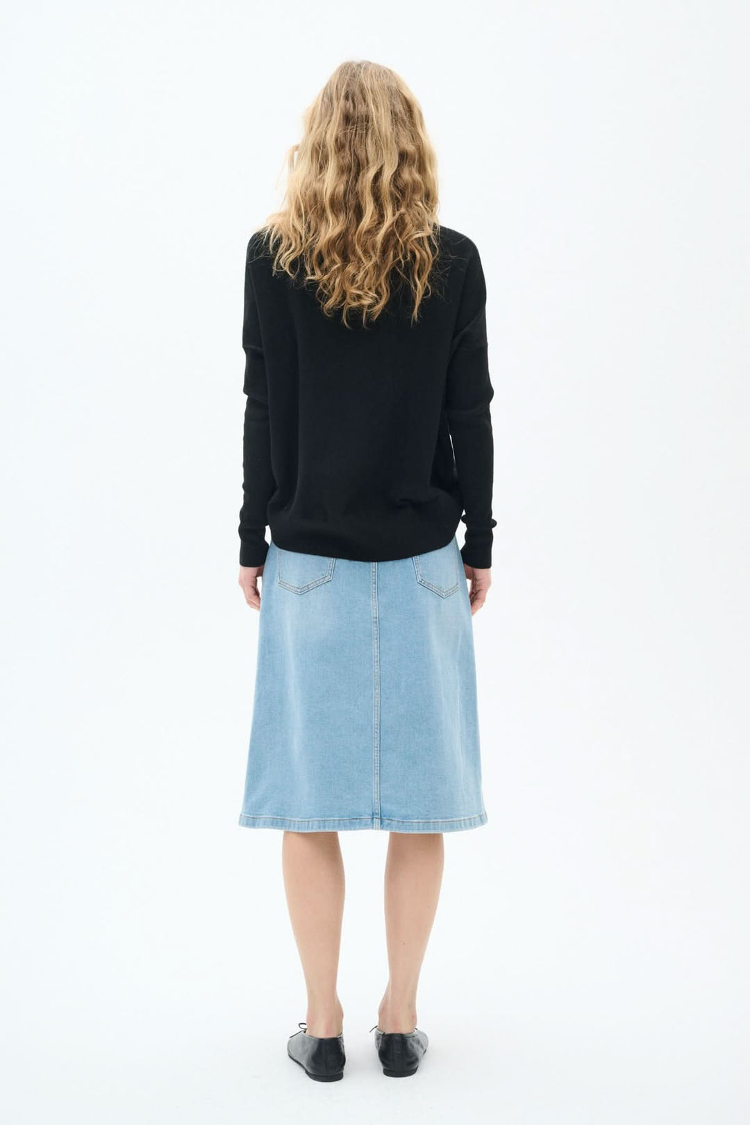 Femme vue de dos portant une jupe en jeans bleu clair classique, longueur midi et pull noir.