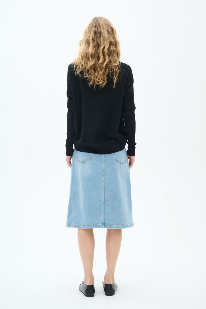 Femme vue de dos portant une jupe en jeans bleu clair classique, longueur midi et pull noir.
