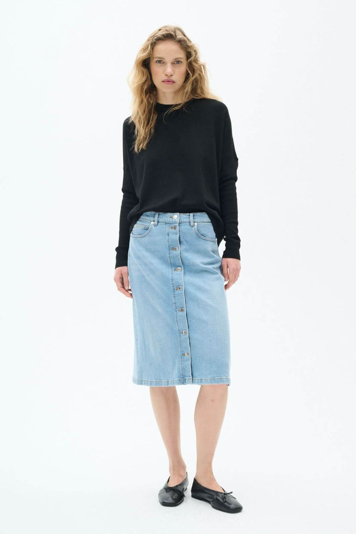 Jupe en jeans bleu clair avec coupe droite, longueur midi, et boutons sur le devant portée par un modèle.