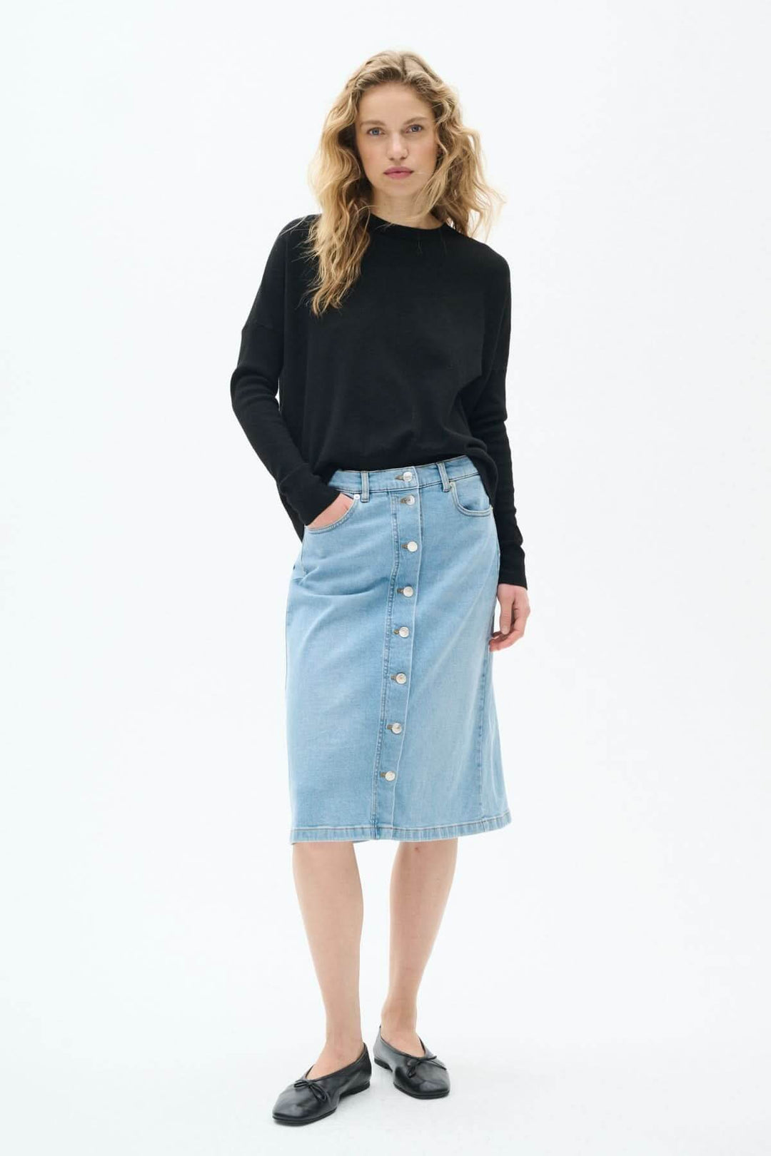 Jupe en jeans bleu clair à boutons avec coupe midi portée par un mannequin en pull noir.
