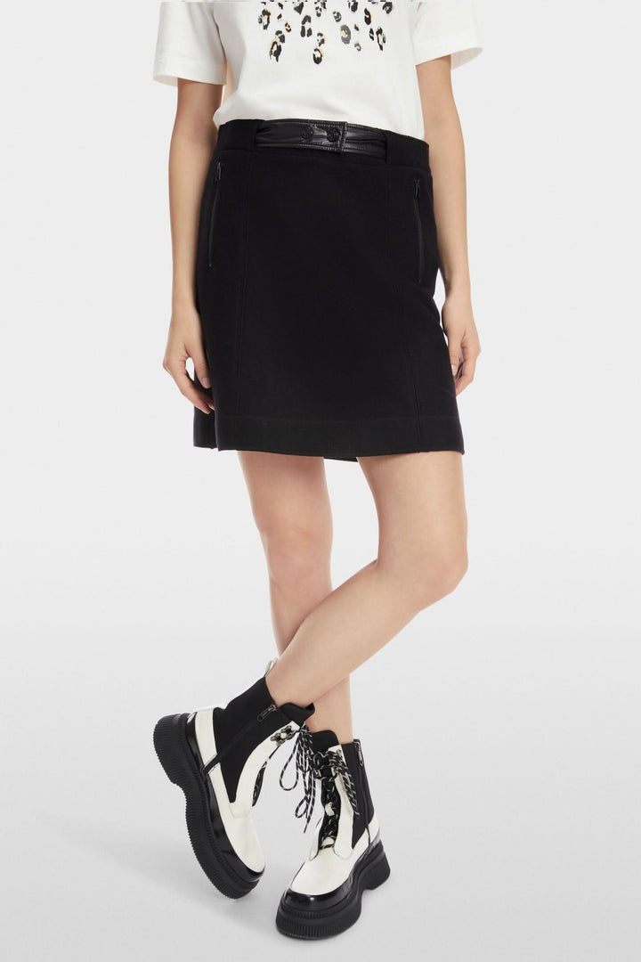 Mini-jupe noire légèrement évasée en laine, portée avec un t-shirt imprimé et des bottes élégantes.