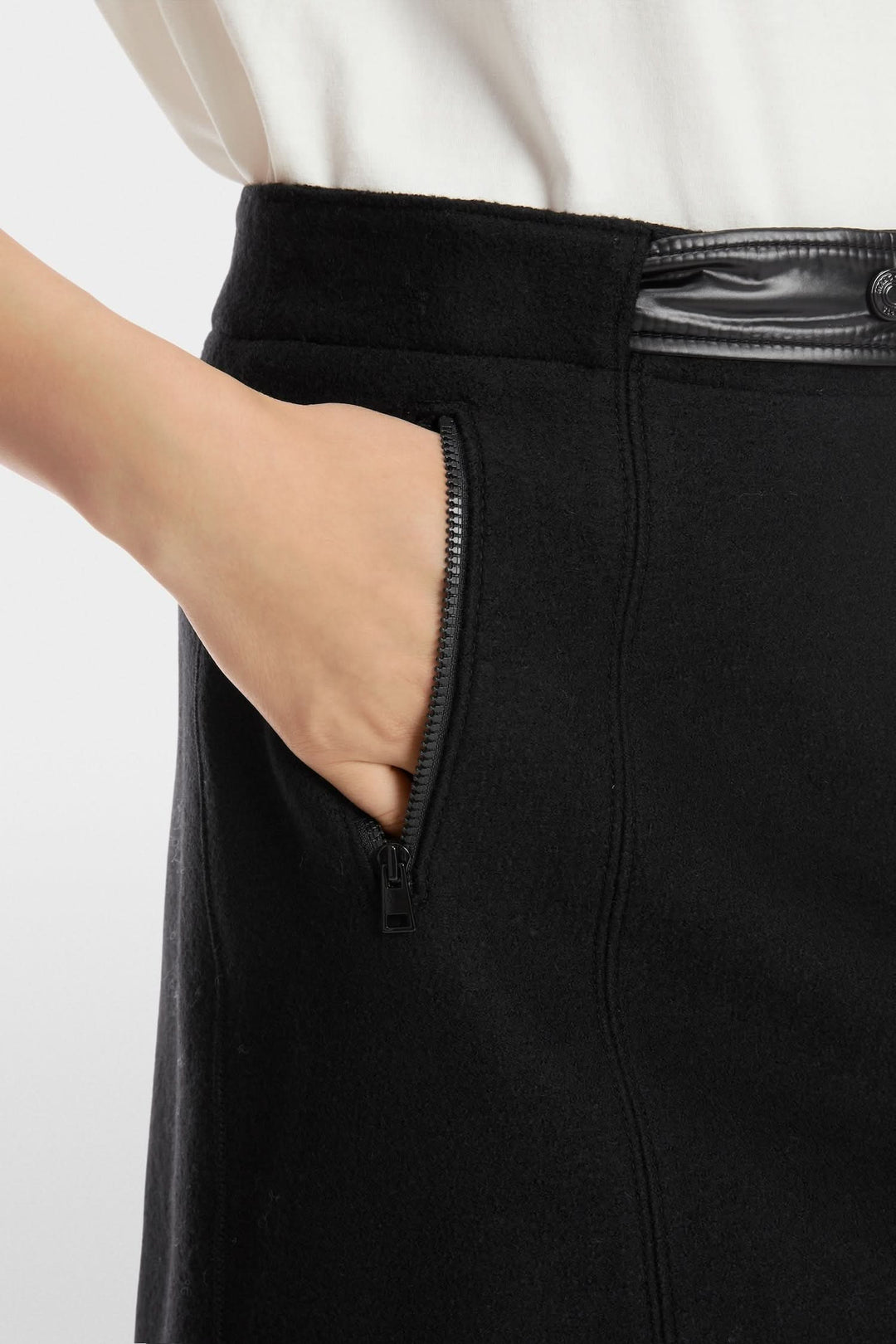 Détail de la mini-jupe en laine tricotée avec une poche zippée et taille élastique en nylon brillant.