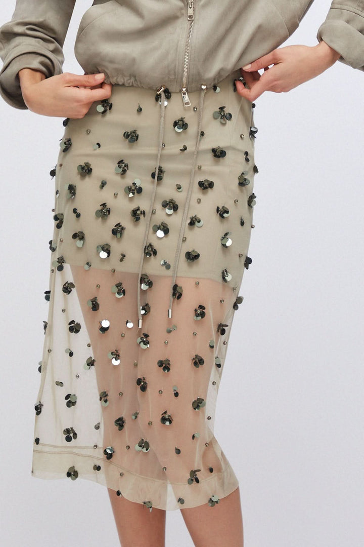 Jupe en maille transparente ornée avec détails appliqués captant la lumière, offrant un effet texturé et moderne.