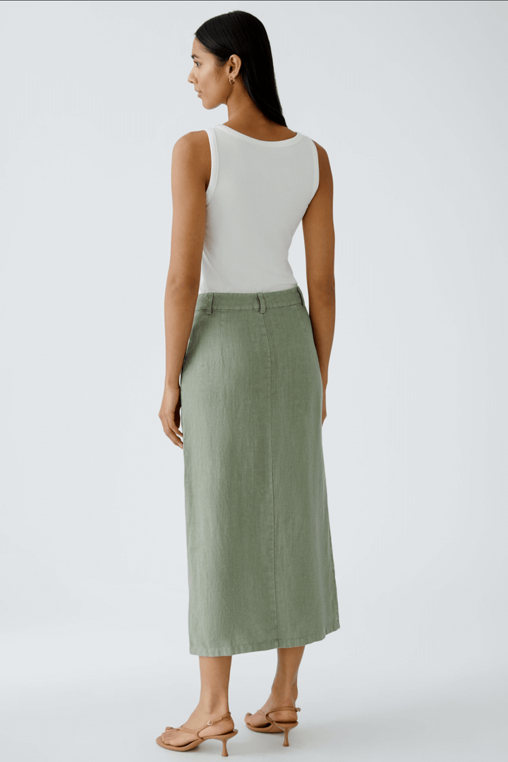 Femme portant une jupe longue en lin olive, vue de dos, avec débardeur blanc et sandals, élégance décontractée.