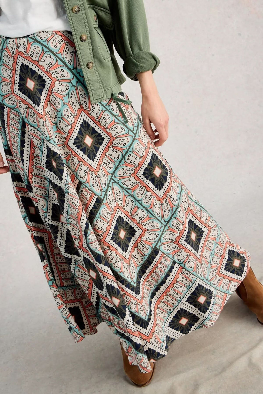 Person wearing jupe longue imprimée fluide avec motifs ethniques et veste verte, illustrant un style estival chic et polyvalent.