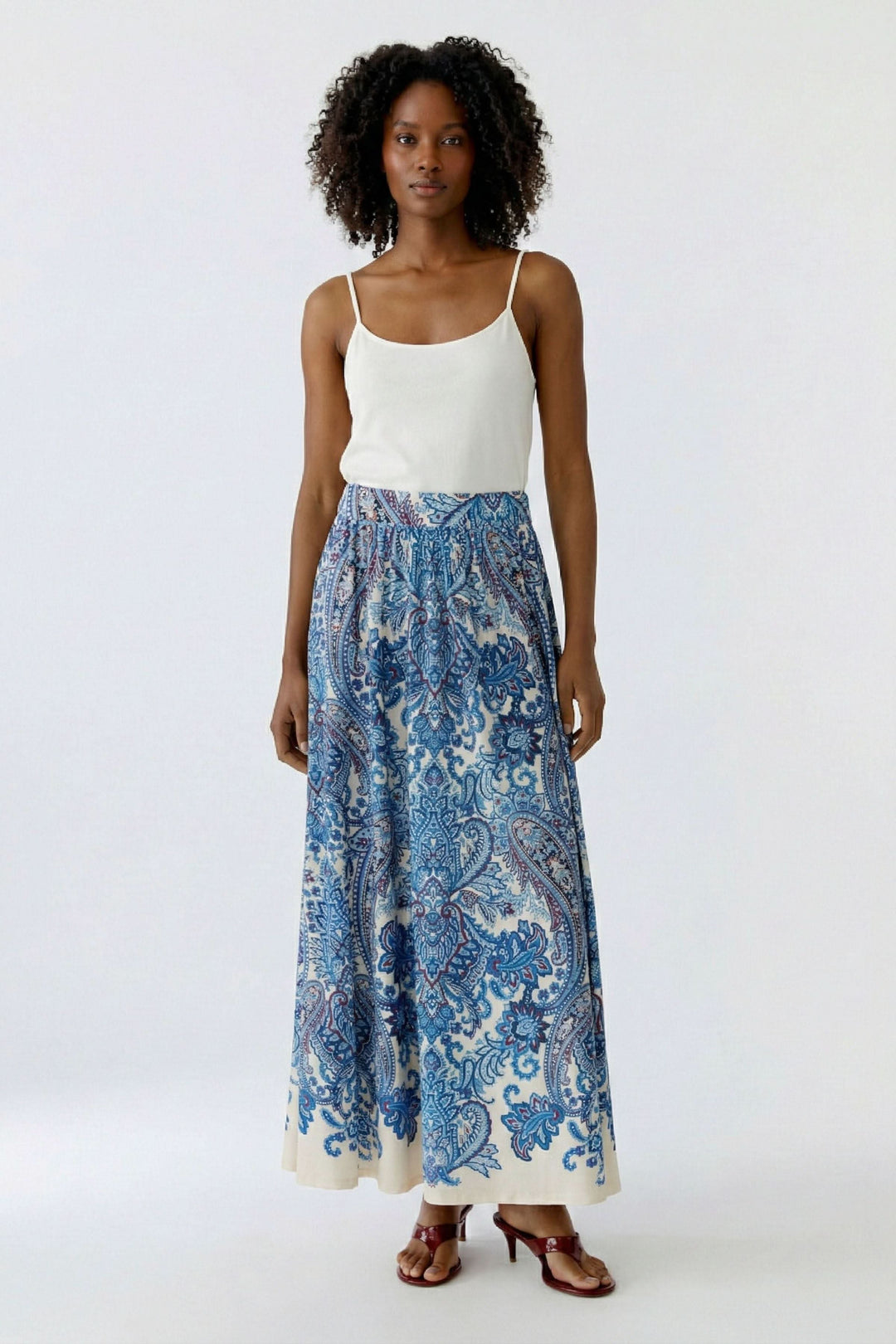 Jupe longue imprimée à taille élastique avec motif cachemire, coupe fluide et élégante, portée par une femme en camisole blanche.