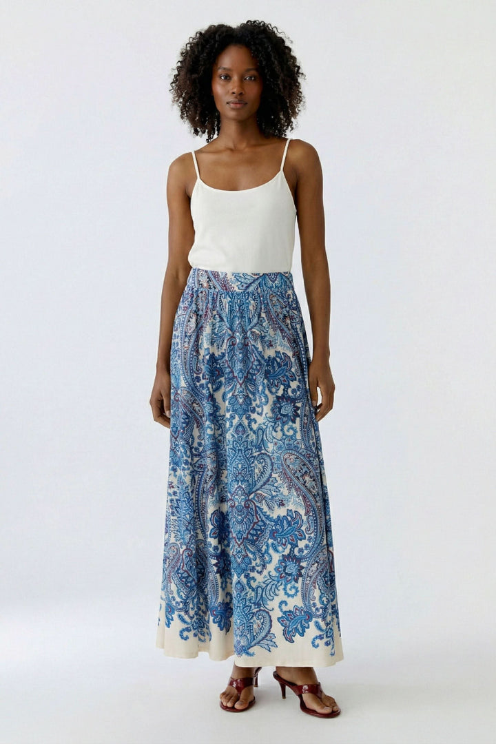 Jupe longue imprimée à taille élastique avec motif cachemire, coupe fluide et élégante, portée par une femme en camisole blanche.