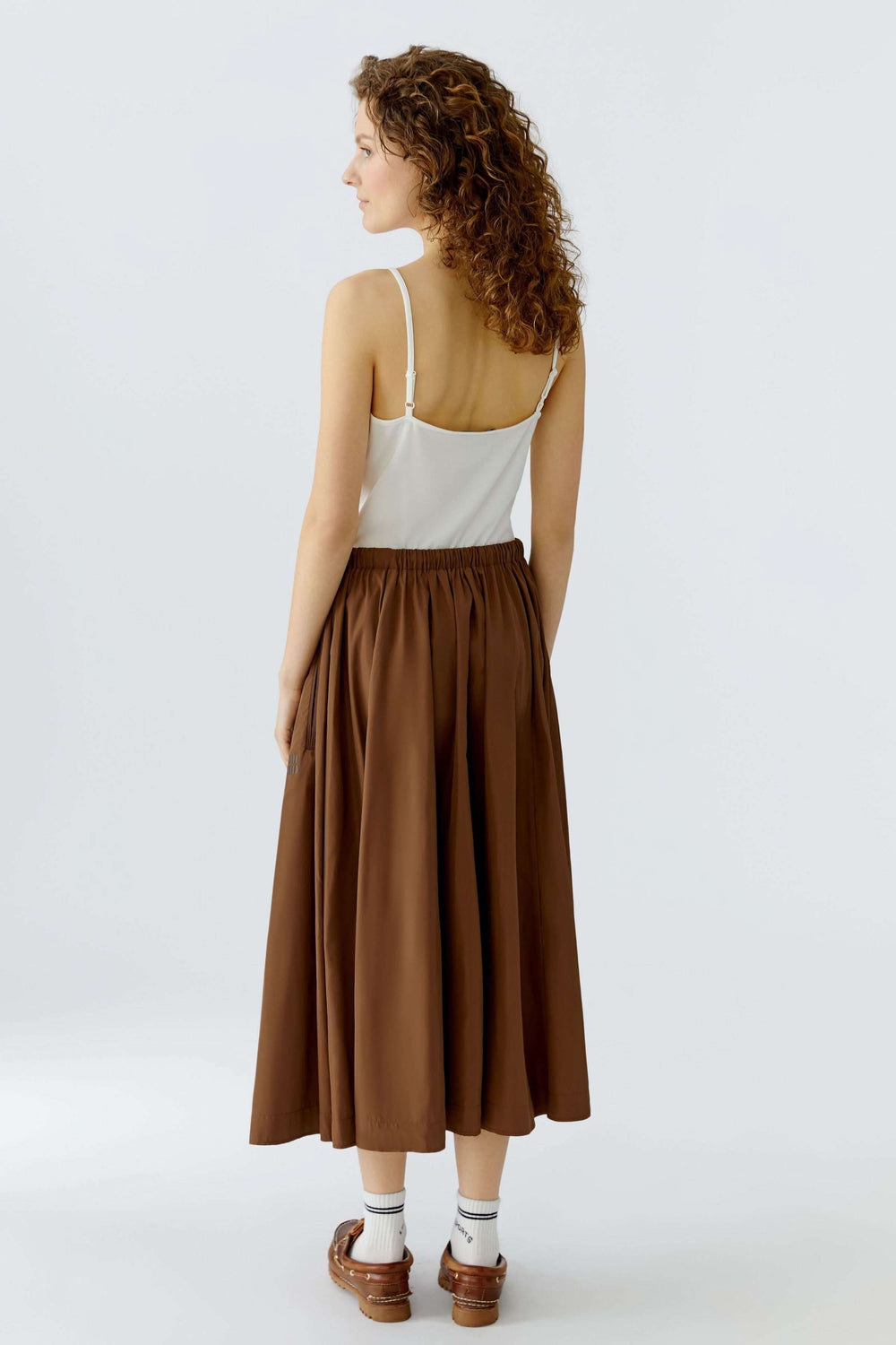 Femme portant une jupe midi fluide marron, vue de dos, mettant en valeur la taille élastique et le mouvement naturel du tissu.