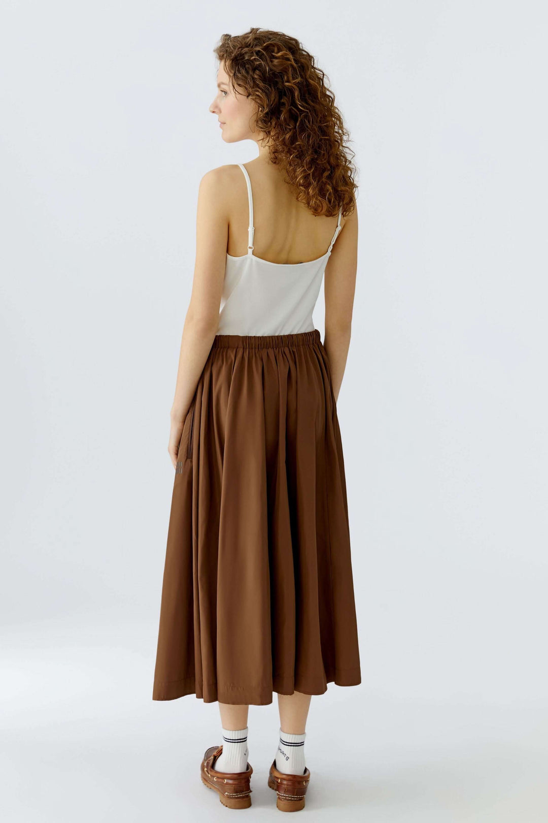 Femme portant une jupe midi fluide marron, vue de dos, mettant en valeur la taille élastique et le mouvement naturel du tissu.