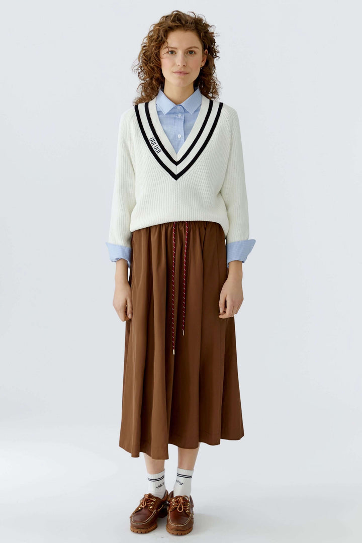 Femme portant une jupe midi fluide marron avec taille élastique et cordon, associée à un pull blanc et chemise bleue.