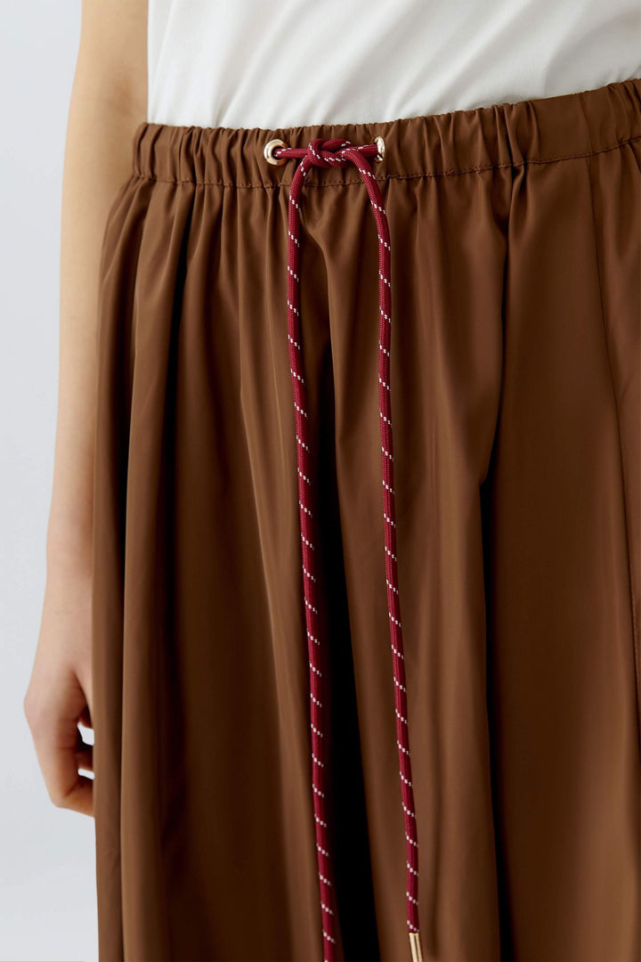 Jupe midi fluide avec taille élastique et cordon ajustable, offrant confort et modernité dans un tissu marron souple.