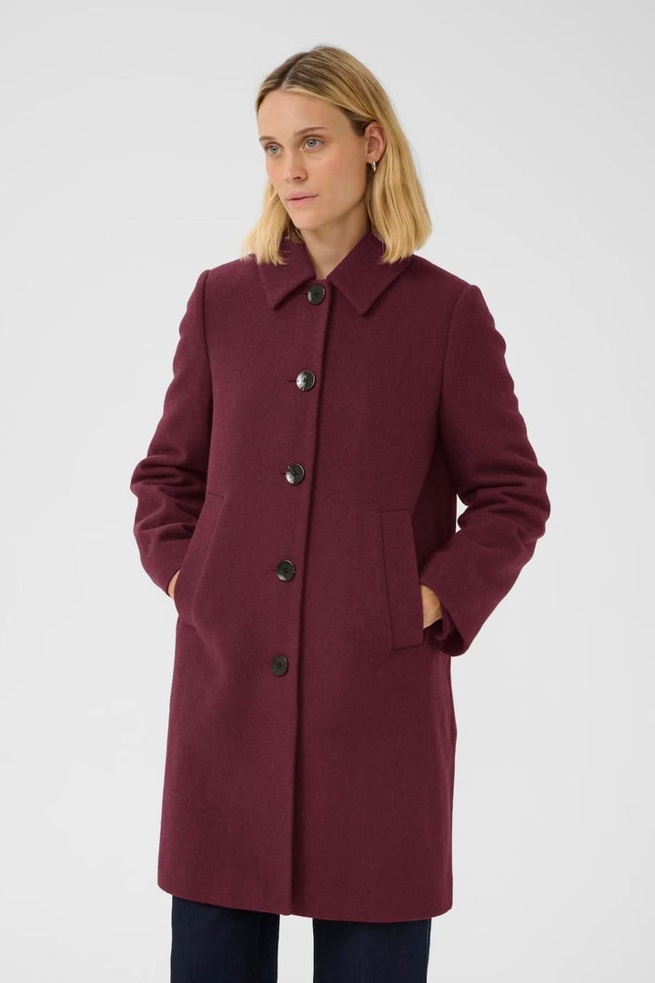 Femme portant le Manteau en laine Kamillas bordeaux avec col chemise, coupe droite et fermeture à boutons, idéal pour l&