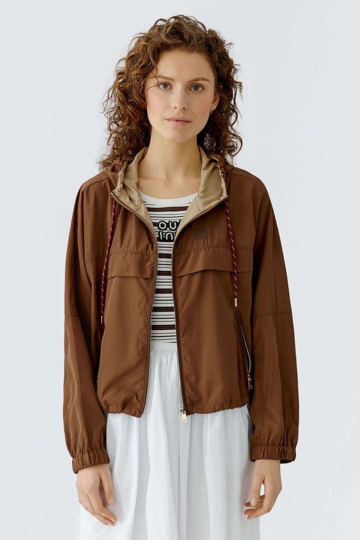 Manteau léger à capuchon marron avec capuchon ajustable, porté par une femme, idéal pour la mi-saison, coupe décontractée.