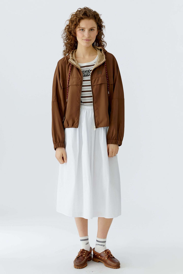 Modèle portant un manteau léger à capuchon marron avec une coupe ample, idéal pour la mi-saison et des tenues décontractées ou urbaines.