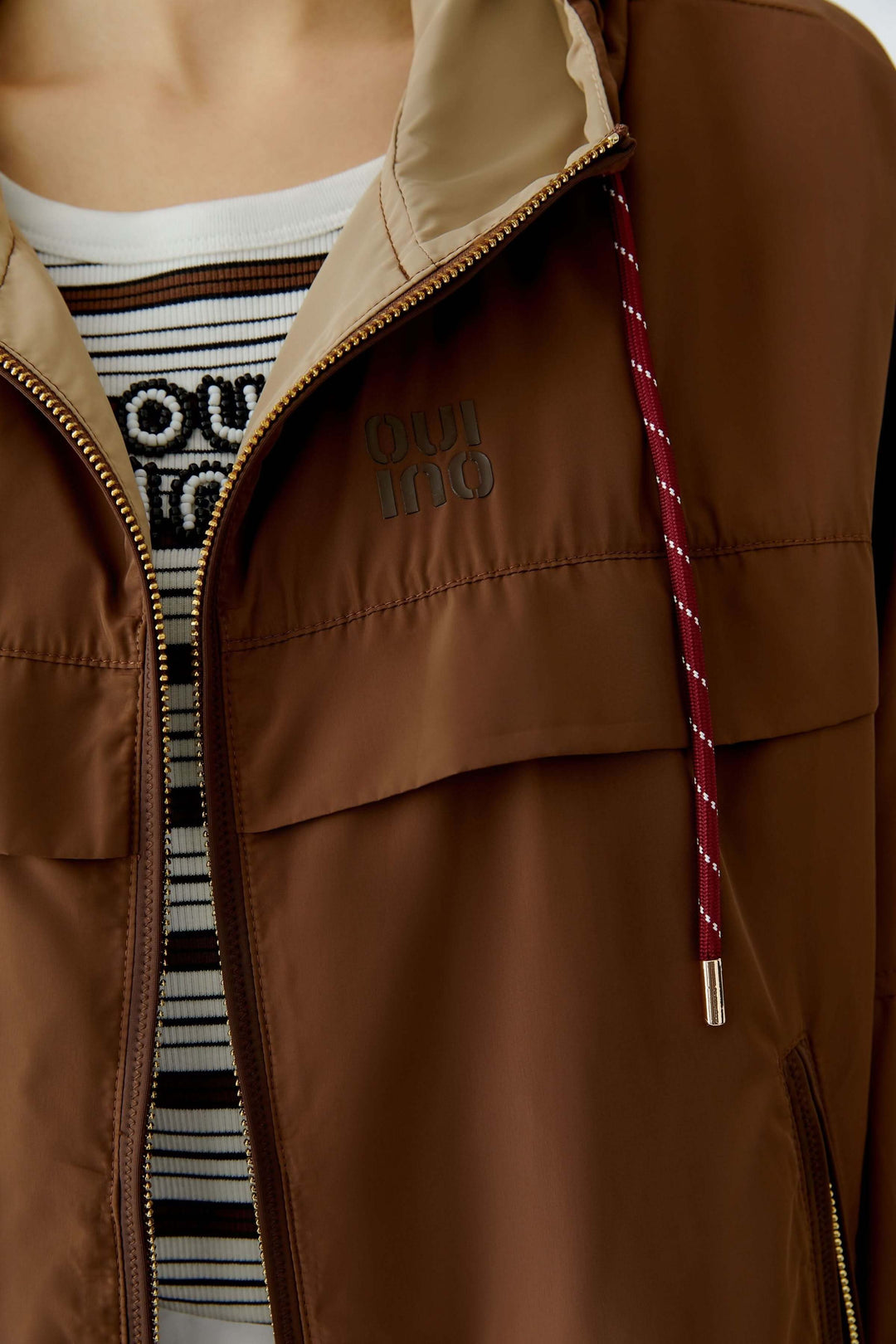 Manteau léger à capuchon marron avec fermeture éclair et détails de cordon rouge, coupe ample pour mi-saison.