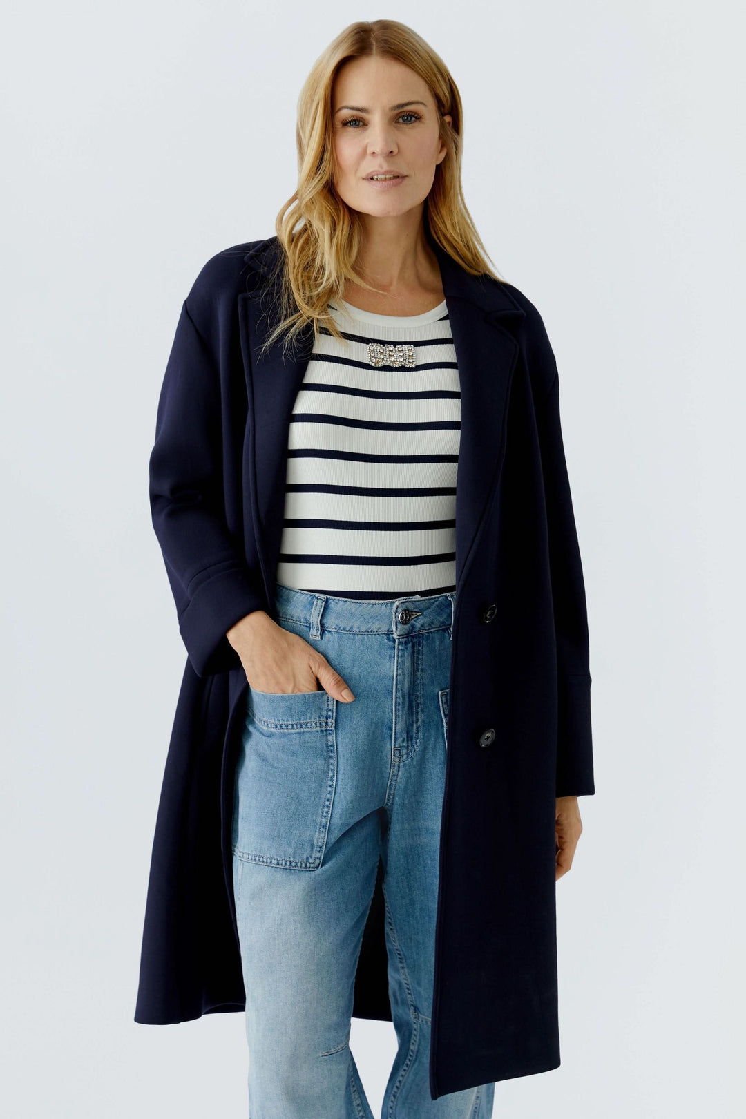 Femme portant un manteau long à coupe droite bleu marine avec un col tailleur. Décontracté et élégant, idéal pour superpositions.