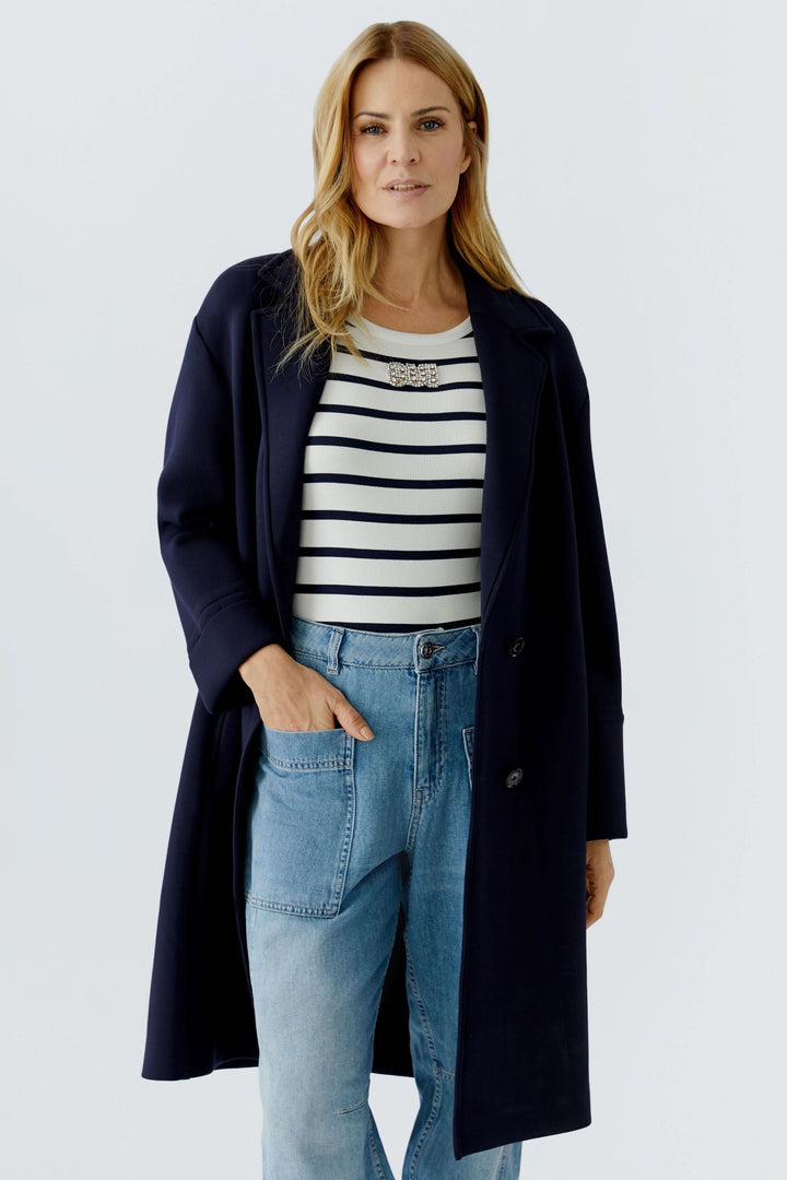 Femme portant un manteau long à coupe droite bleu marine avec un col tailleur. Décontracté et élégant, idéal pour superpositions.