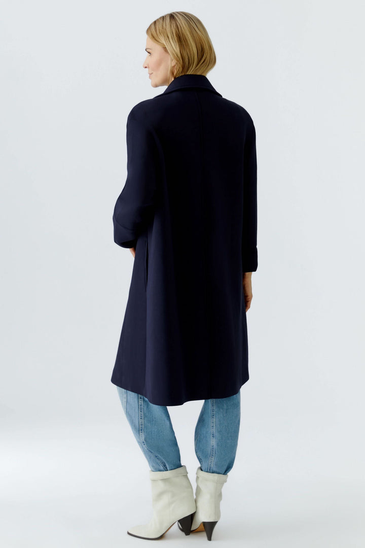 Femme portant un manteau long à coupe droite avec col tailleur classique, style polyvalent, vue de dos.
