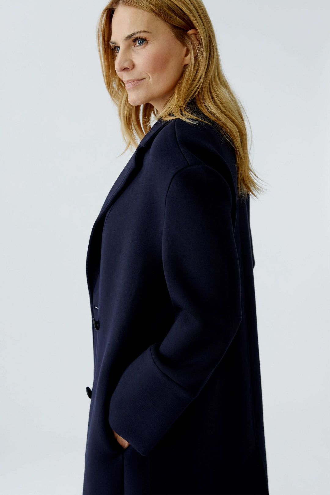 Femme portant un manteau long à coupe droite avec col tailleur classique, design épuré pour une élégance polyvalente et structurée.