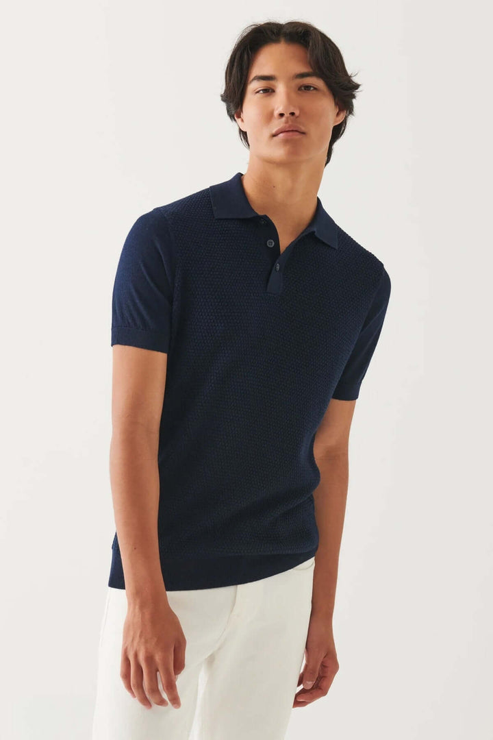 Homme en polo bleu marine, coupe moderne, porté avec un pantalon blanc, mettant en avant le style élégant et décontracté.