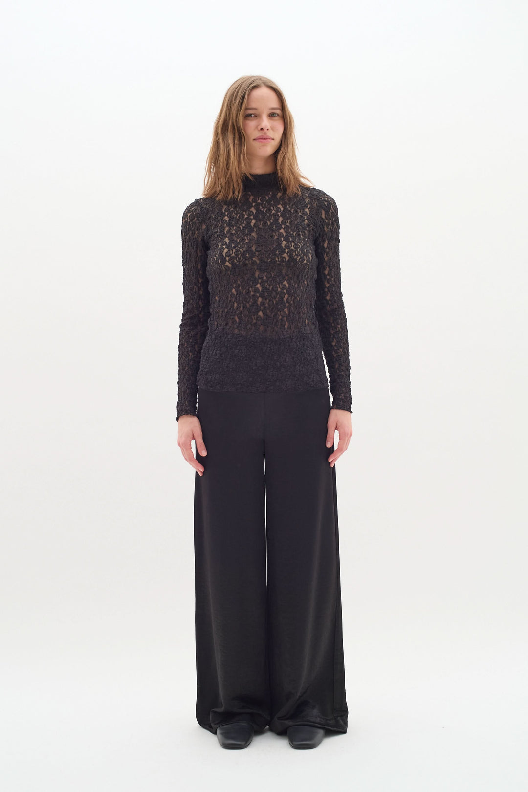 Femme en pantalon Didra noir satiné, look chic et minimaliste, avec top en dentelle. Coupe droite et taille haute pour élégance.