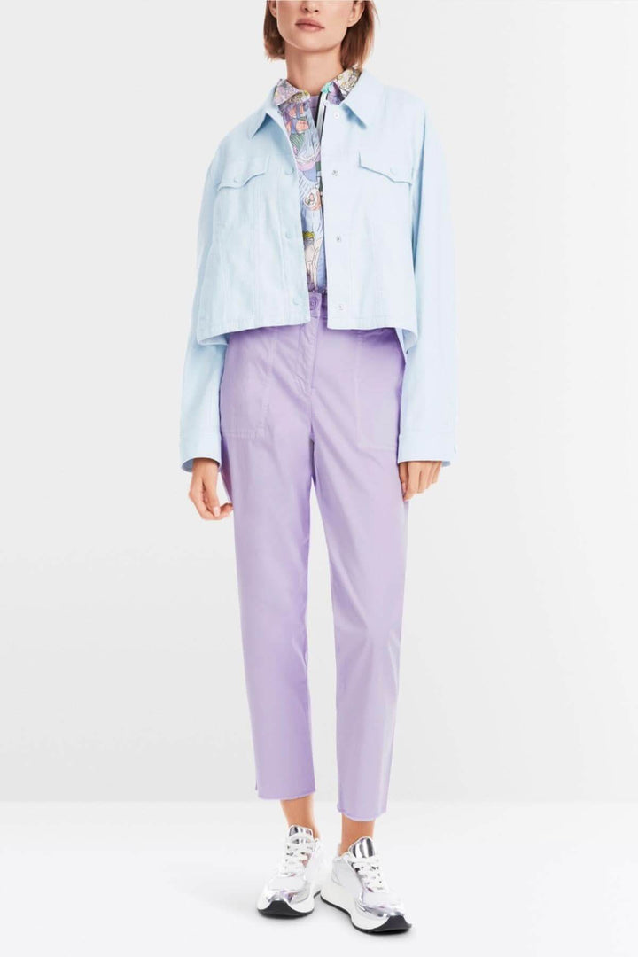 Femme portant une veste en jean bleu et un pantalon lilas, style décontracté et moderne, avec des chaussures blanches.