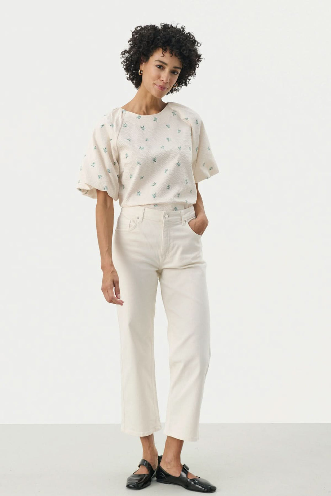 Femme avec t-shirt à motifs et pantalon évasé blanc, style décontracté et moderne, posture élégante.